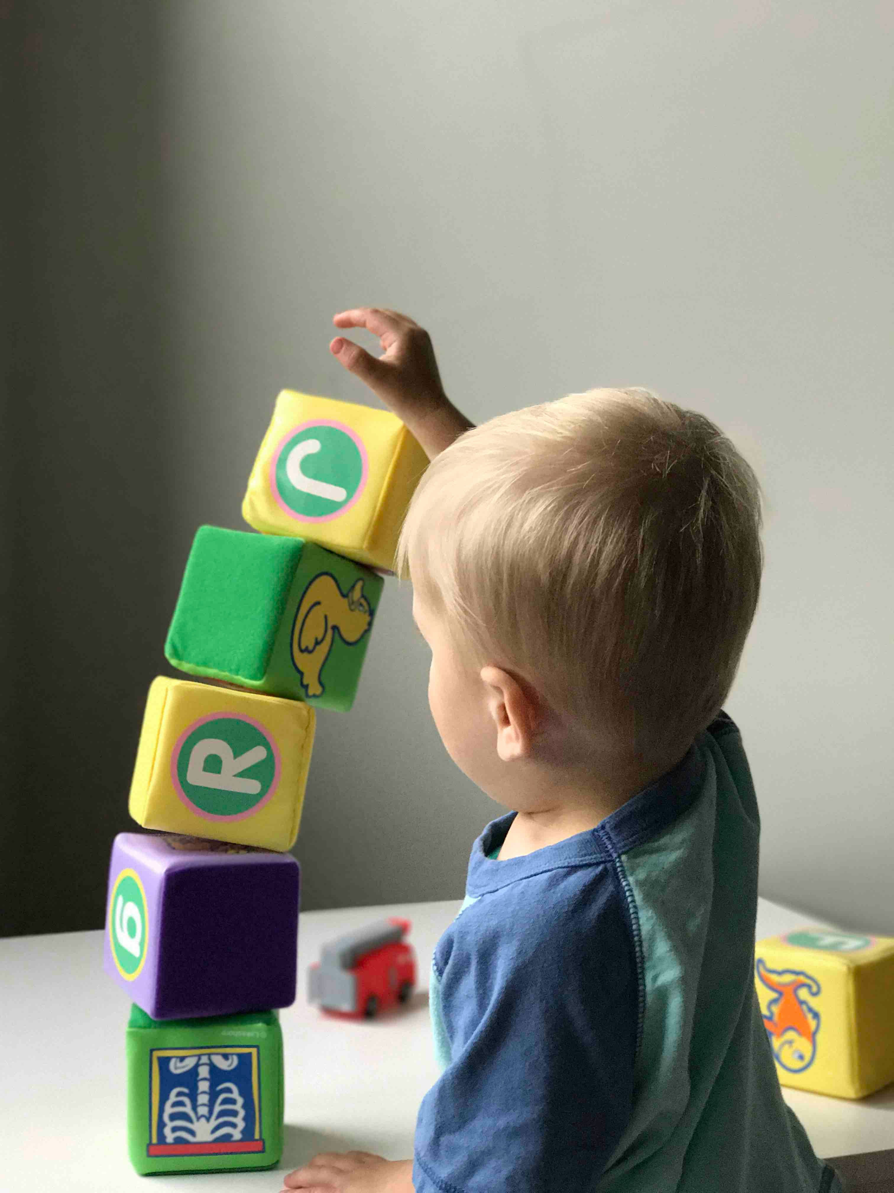 A toddler reaching up to stack soft alphabet blocks