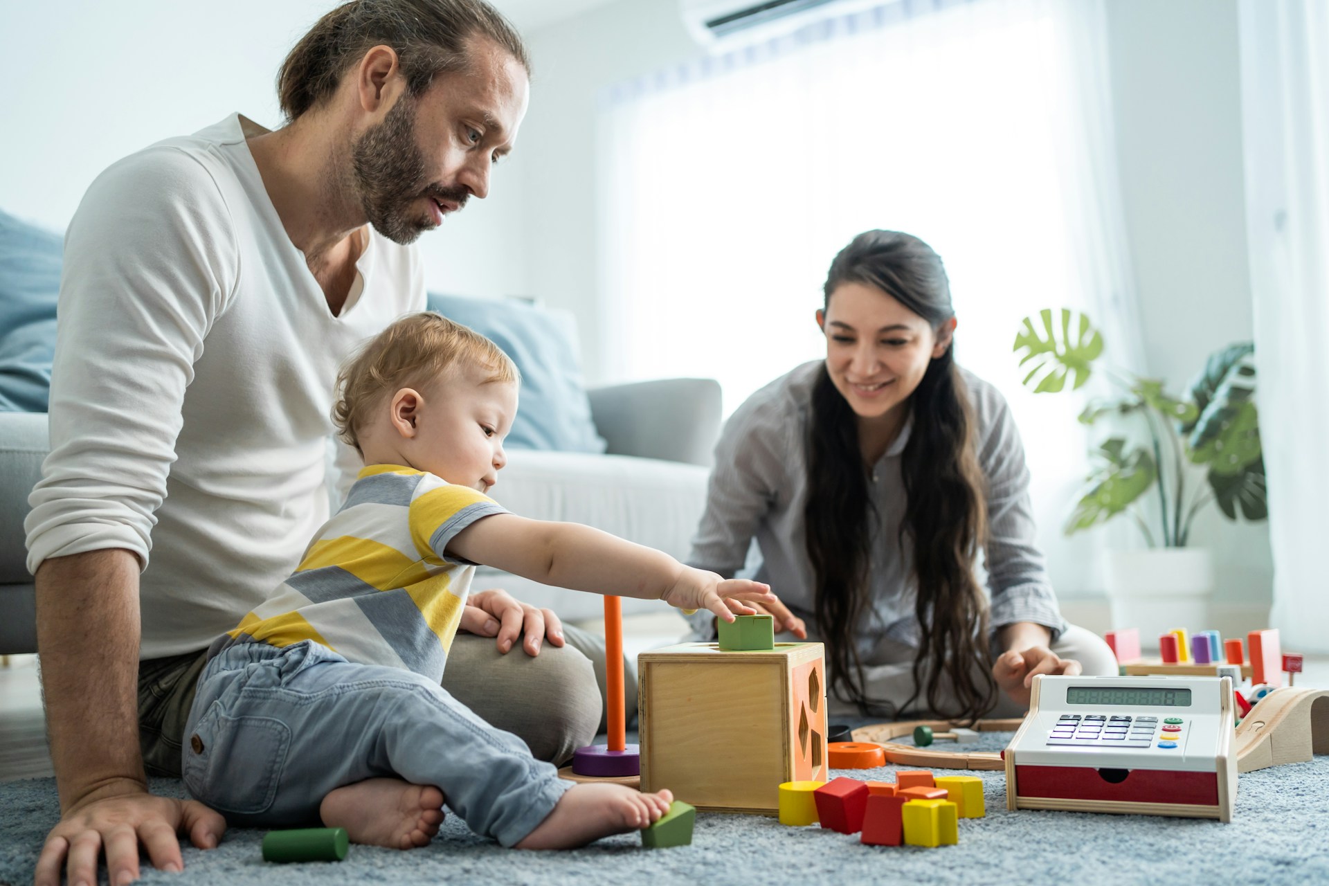 A father and daughter putting coins into a piggy bank on a coffee table, while a pregnant mother looks on from the sofa